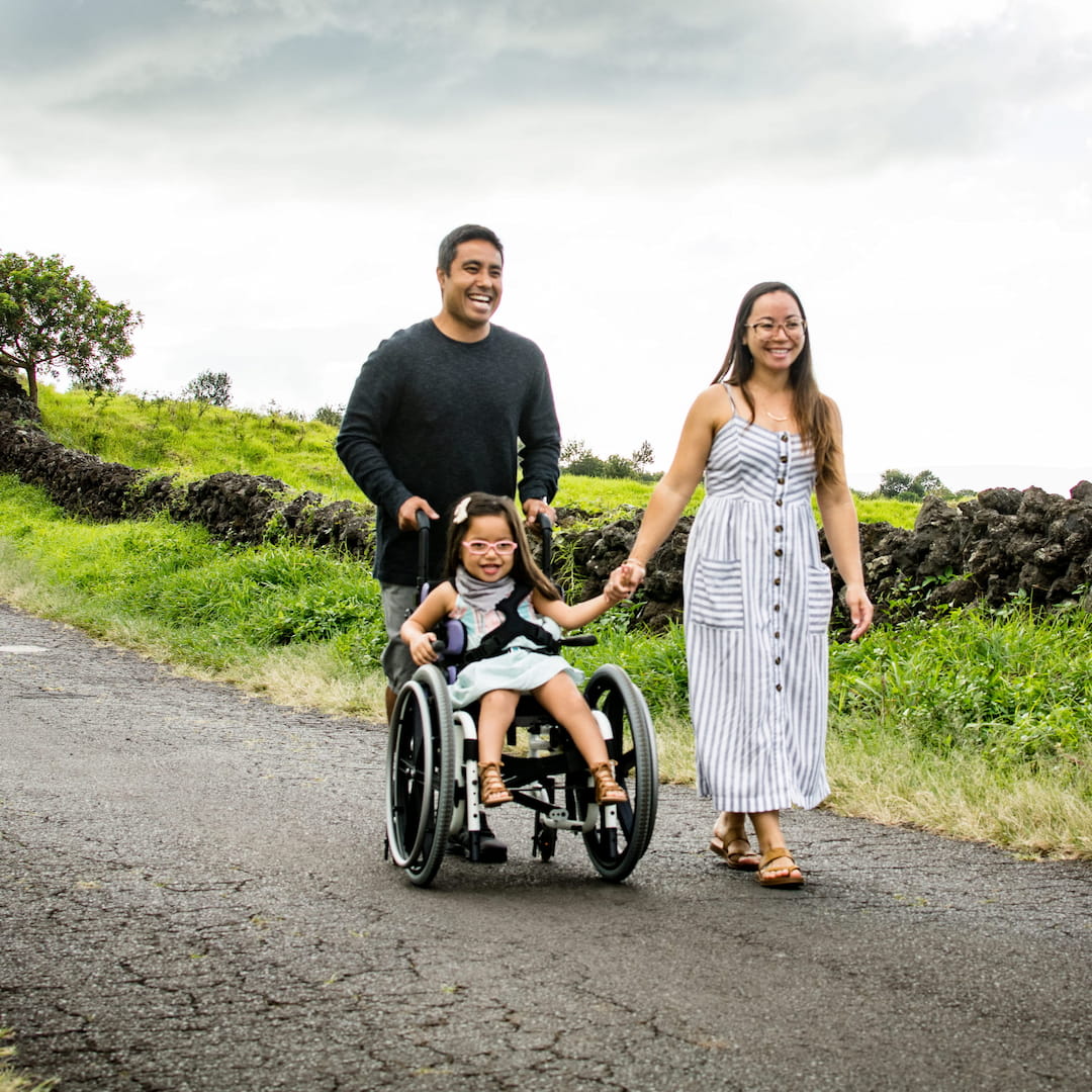 Family happily walking with their daughter in a wheelchair provided by Gammie